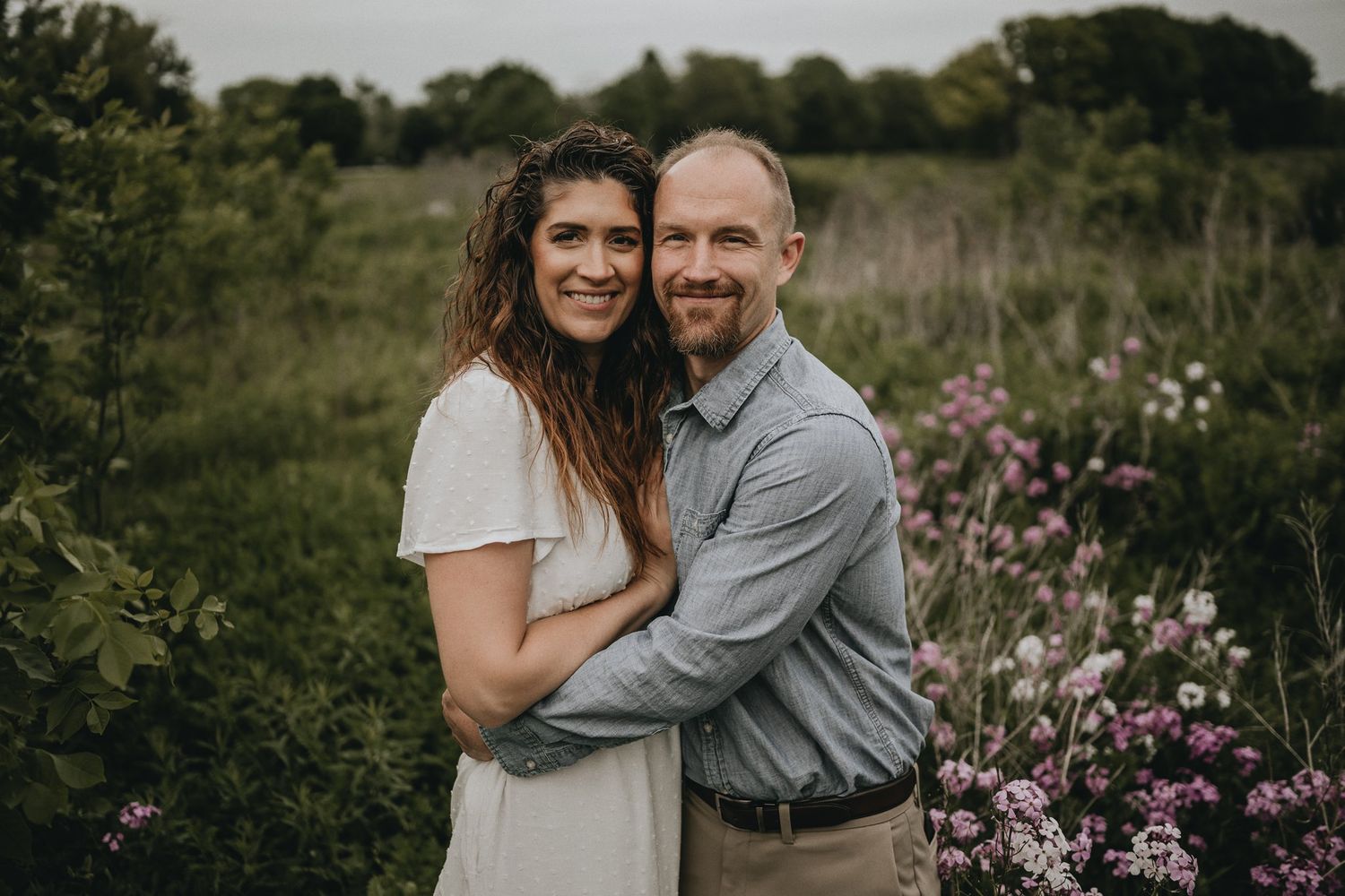 A romantic outdoor portrait surrounded by pink wildflowers and natural foliage.