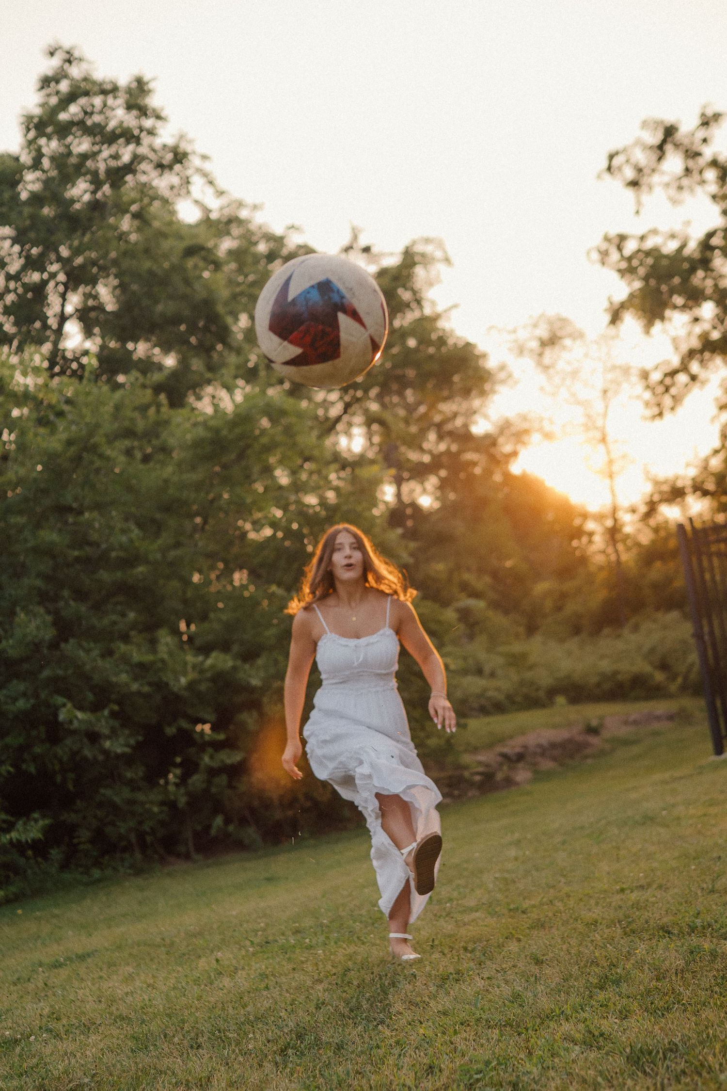 Athletic pose with volleyball against sunset in flowing white dress.
