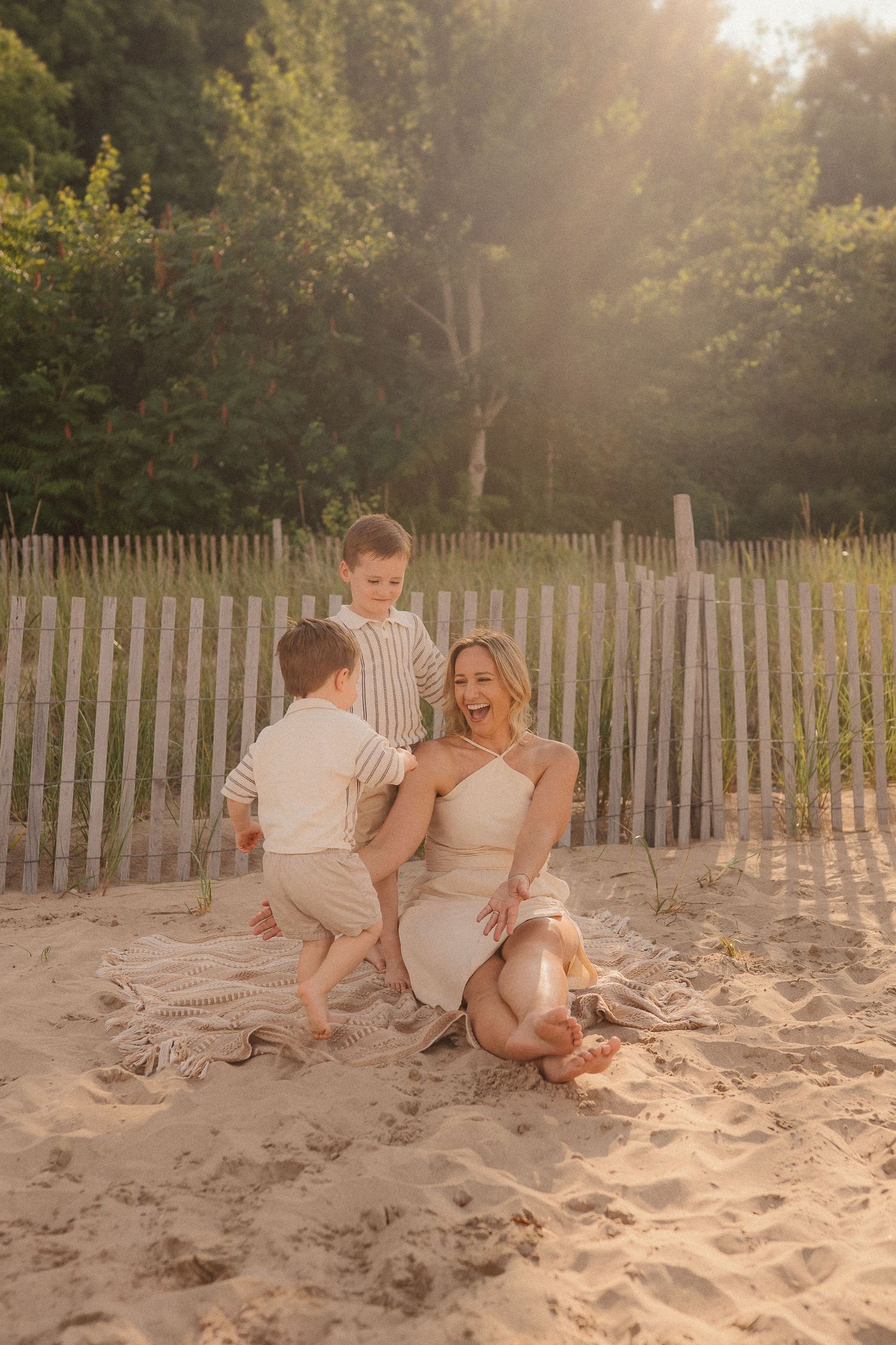 People enjoy a sunset moment together on a sandy beach with a wooden fence in the background.