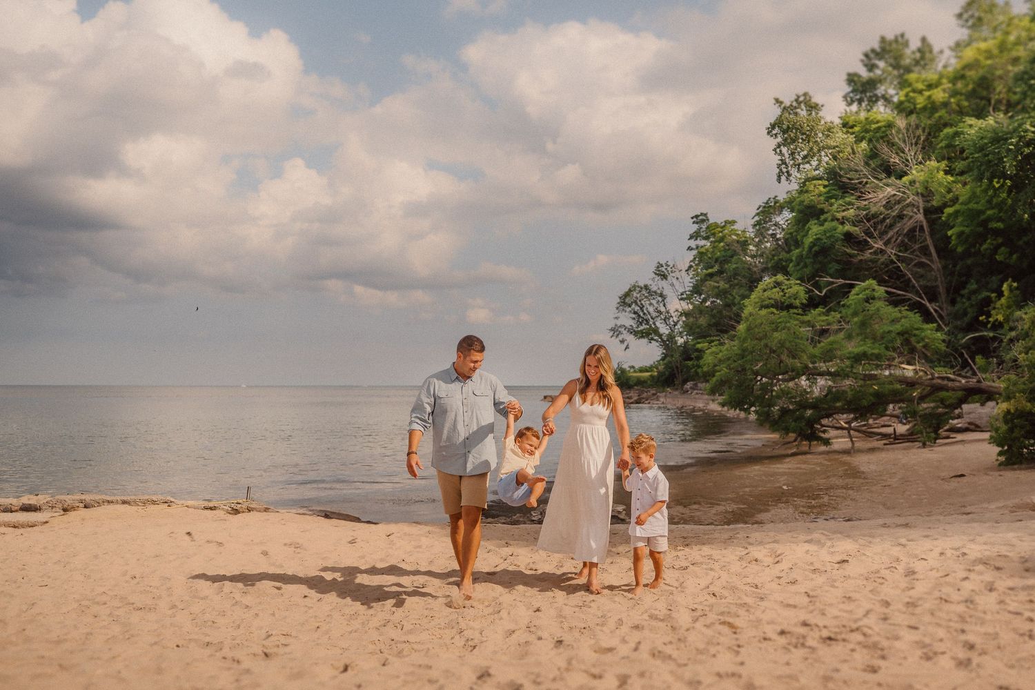 Family walking along a scenic beach at sunset with golden light and clouds in the sky.
