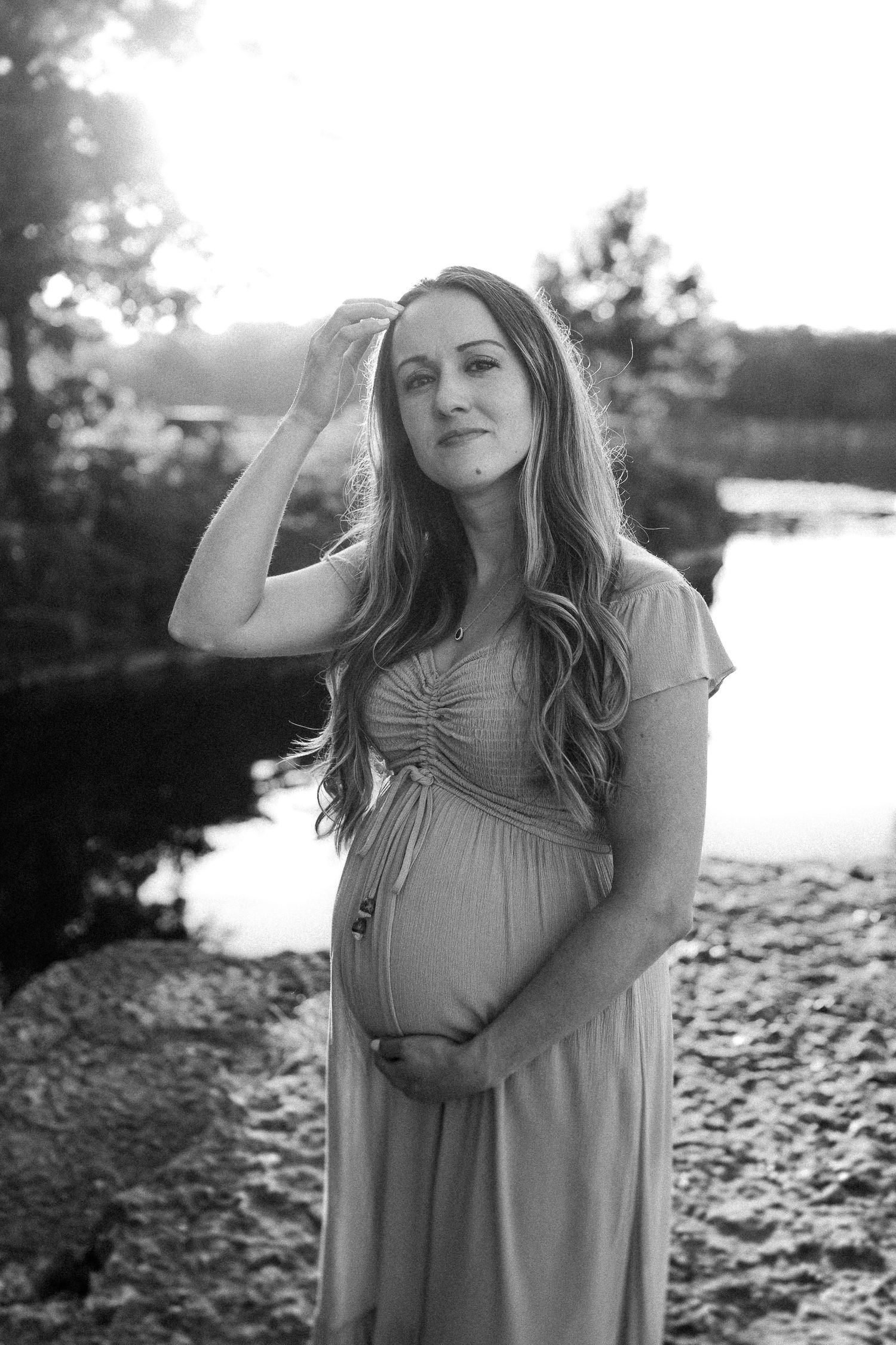 Black and white portraits of a woman in a flowing dress against a waterfront background during sunset.