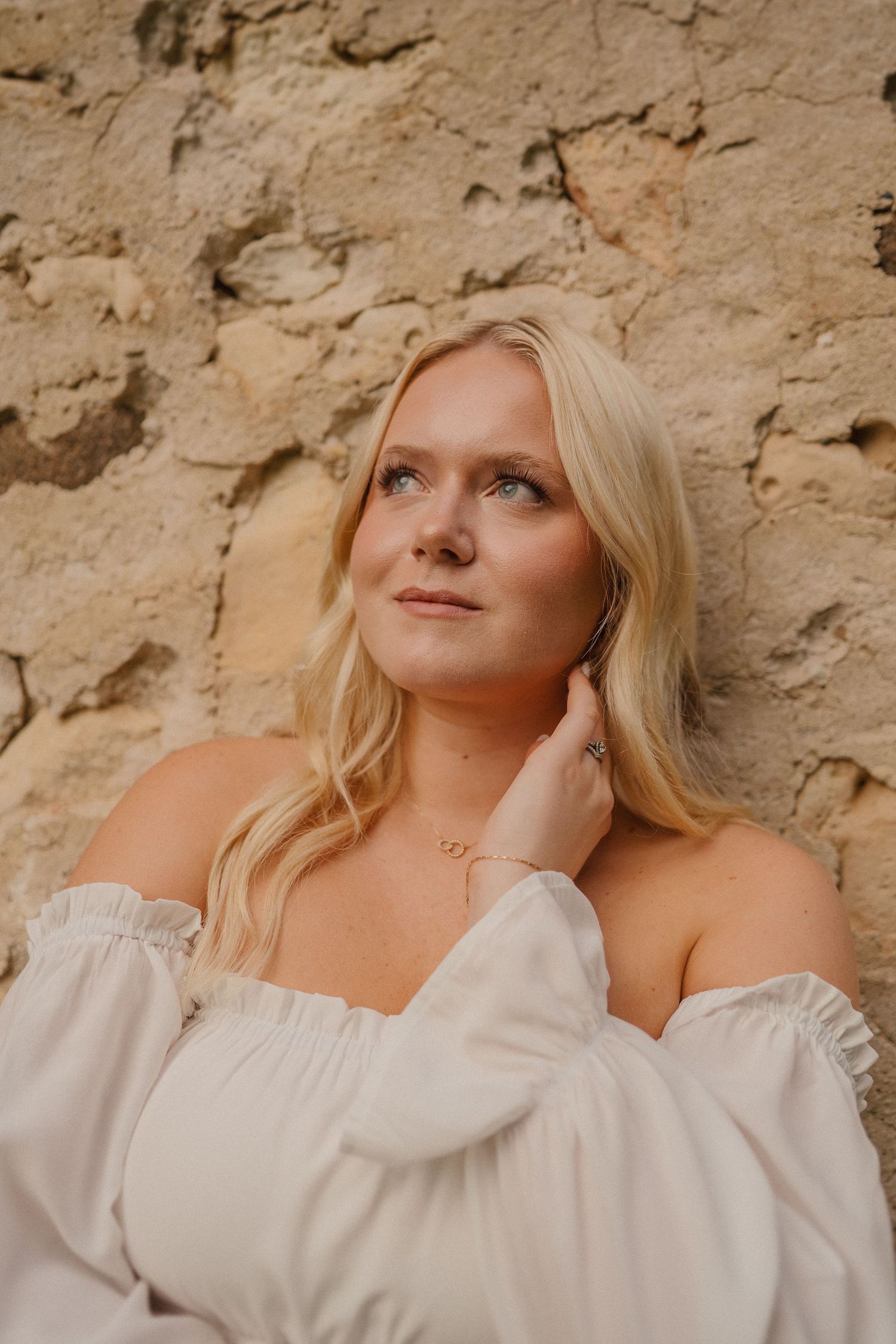 Romantic off-shoulder white dress styled against weathered stone wall background.