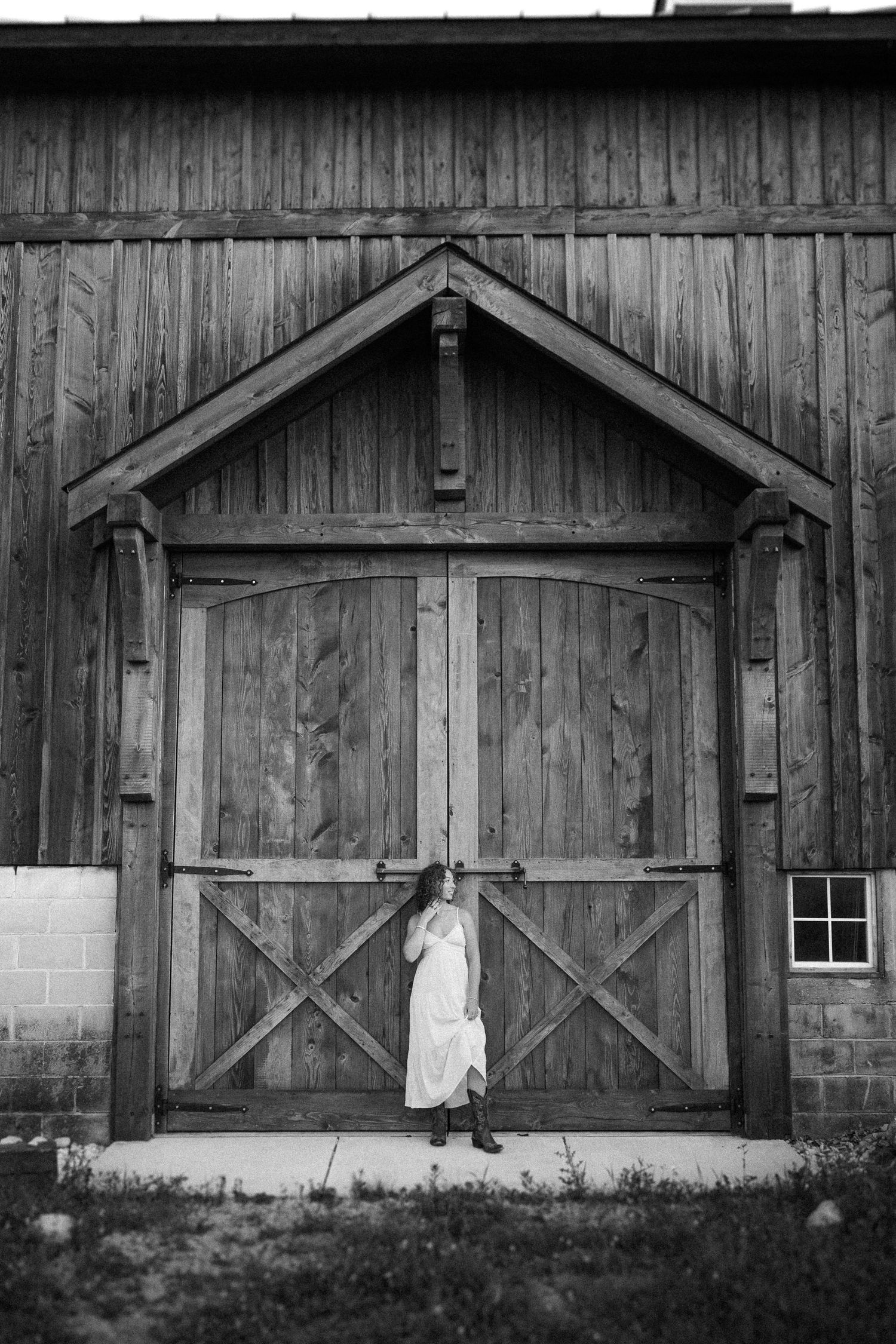 A rustic black and white photo of someone in white standing against a wooden barn door.