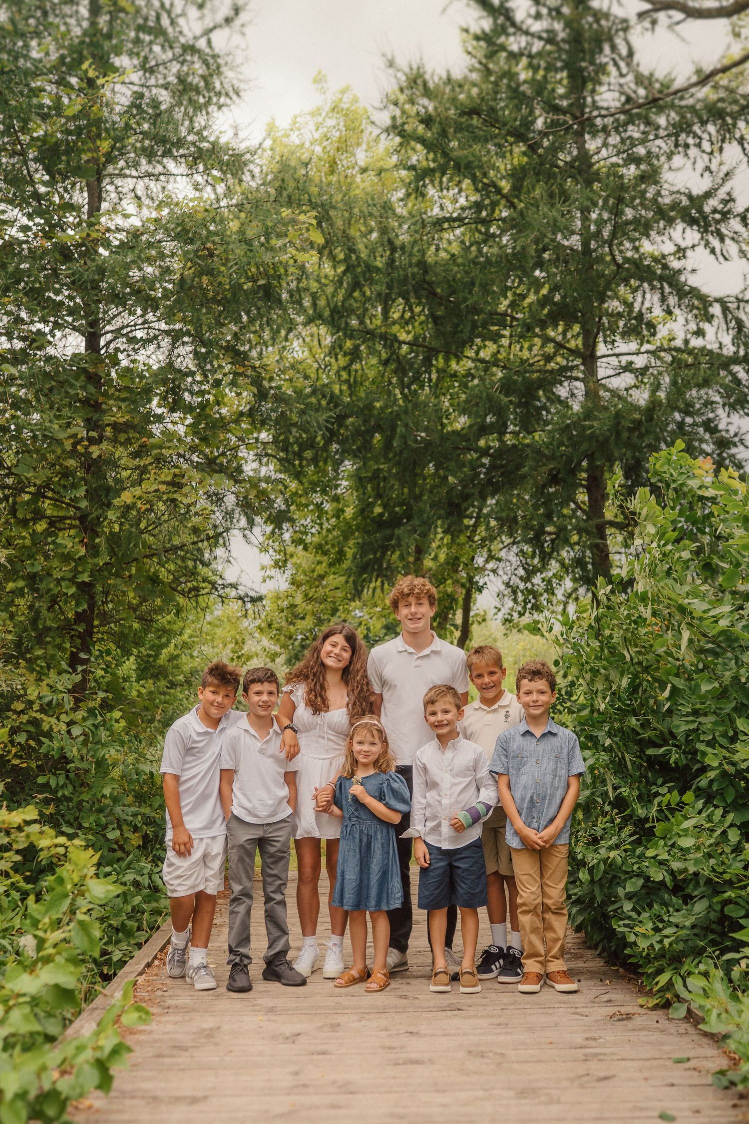 Group poses together on a garden path surrounded by lush green trees and foliage on a summer day.