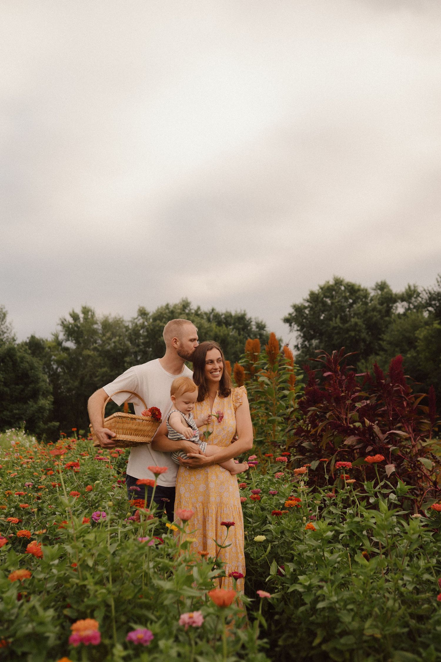 Couple sharing tender moments while picking flowers in a vibrant garden field during overcast weather.