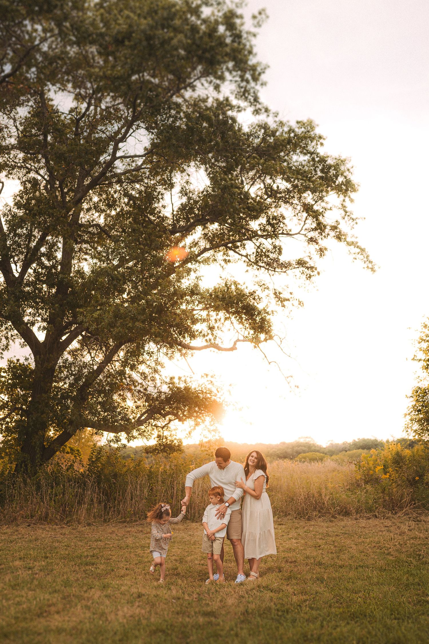 Family silhouetted against a large tree during golden hour in a meadow.