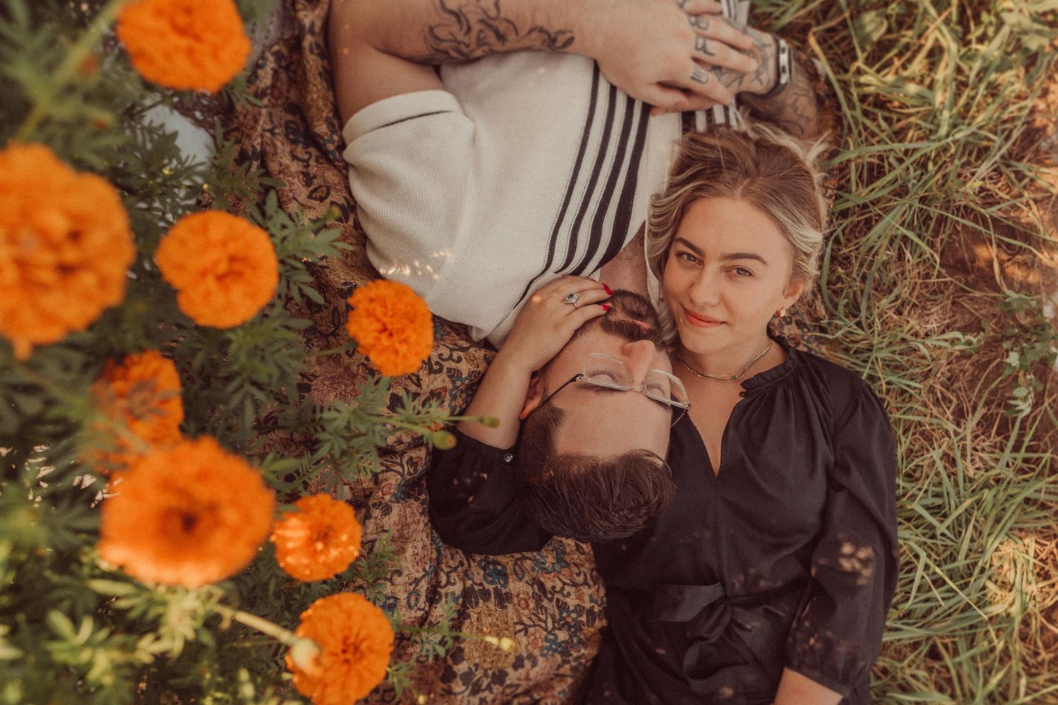 A couple lies among bright orange marigolds in a garden setting.