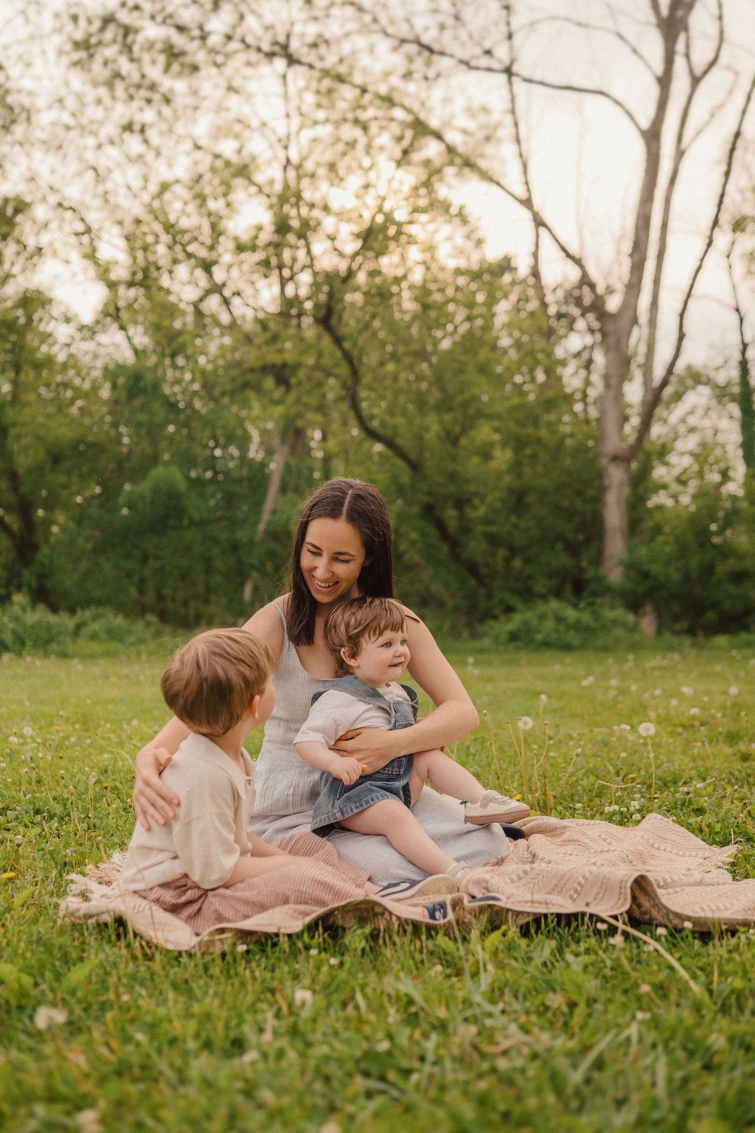 A tender outdoor family moment on a blanket in a grassy field during golden hour.