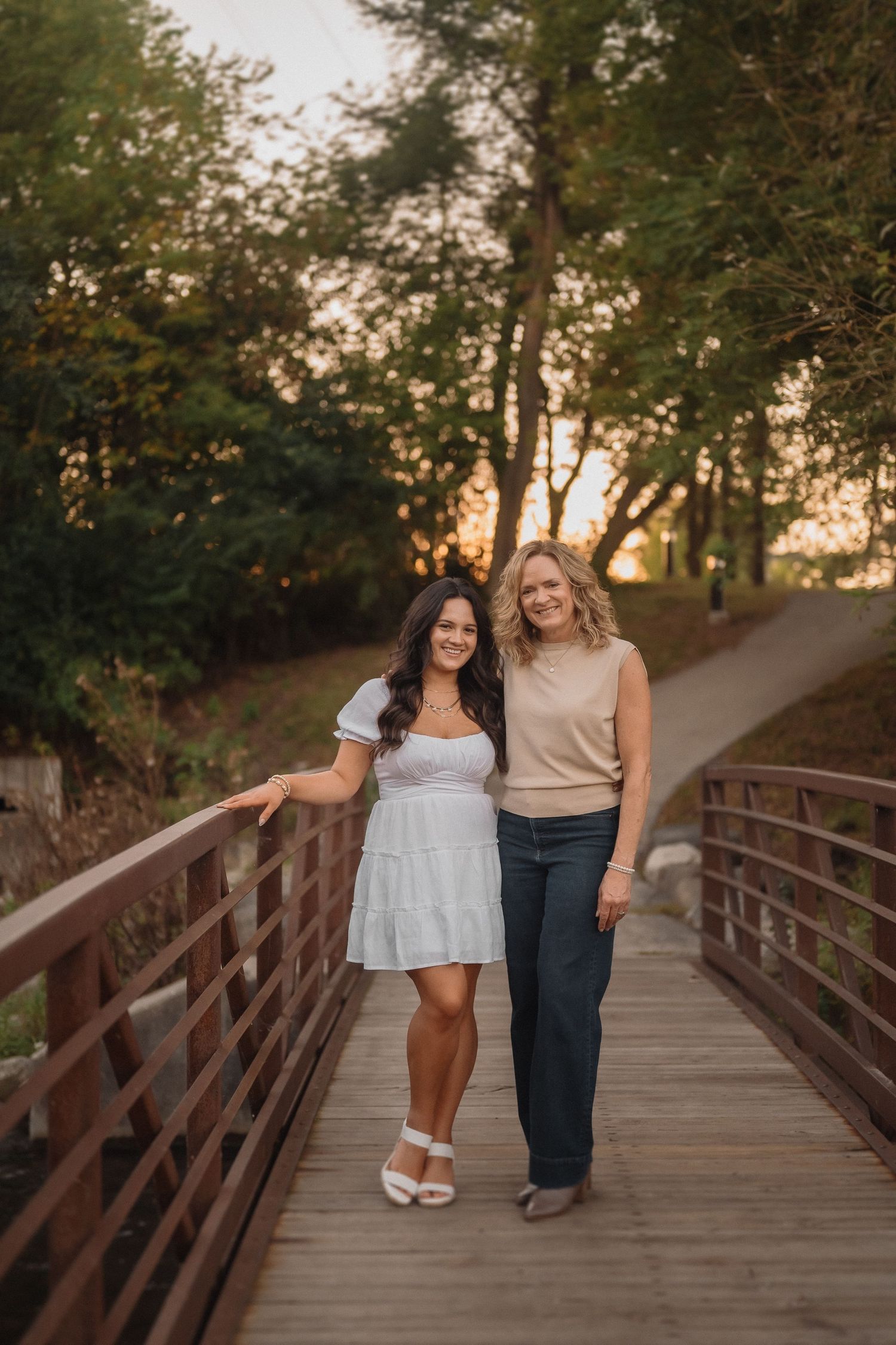 Two friends sharing a moment while walking on a wooden bridge during golden hour sunset.