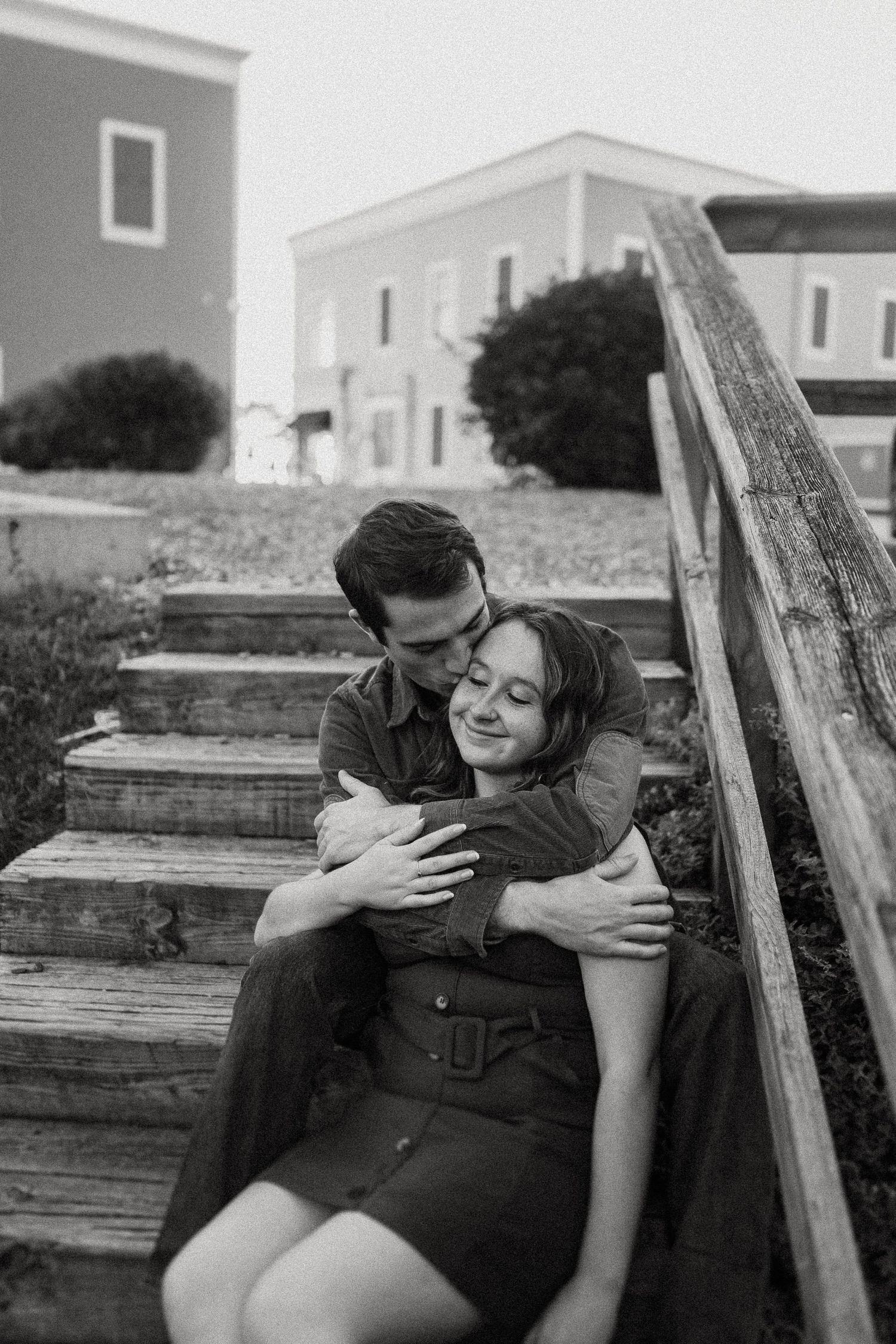 A black and white portrait of a couple embracing on wooden steps.