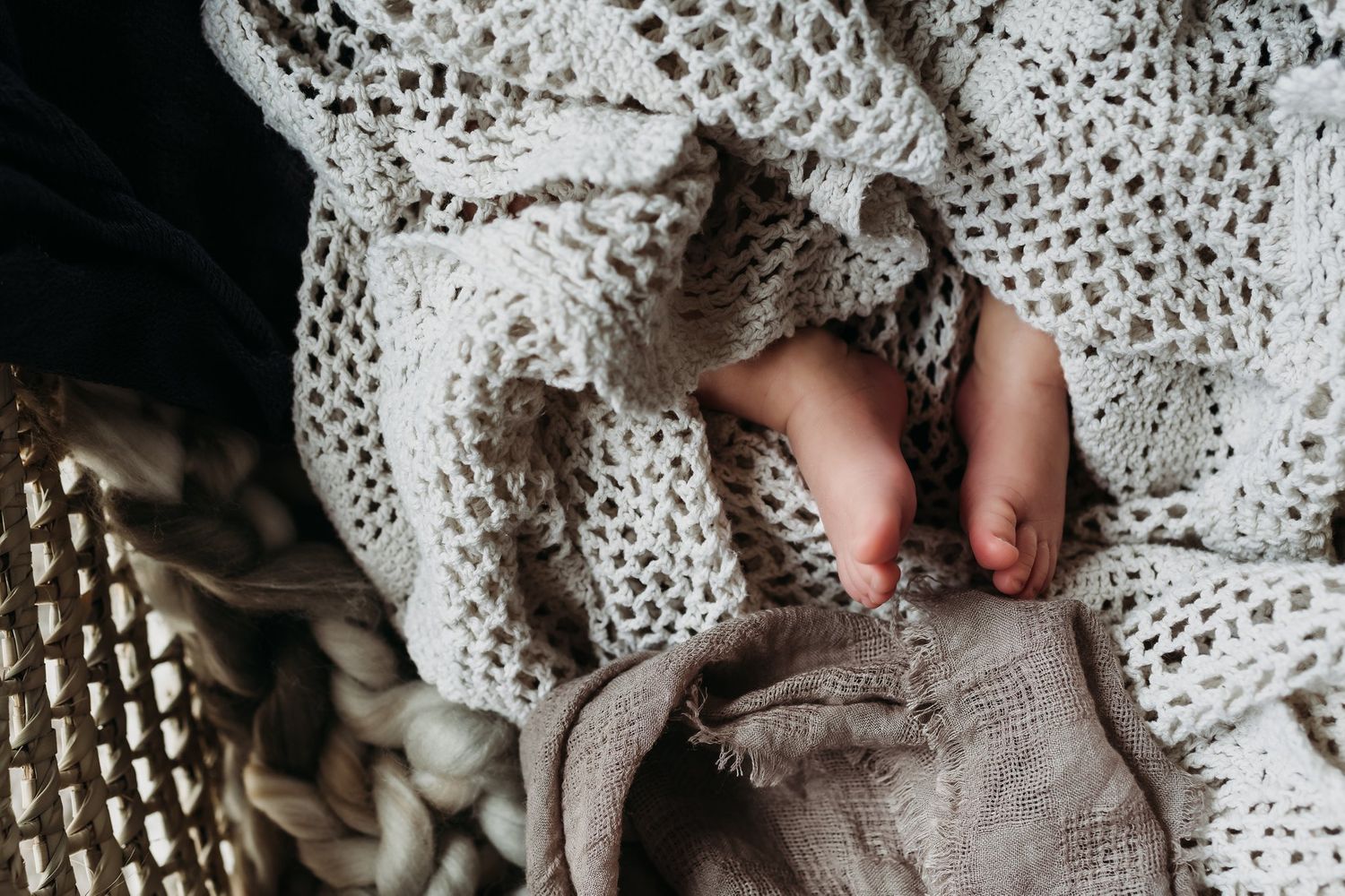Tiny baby feet peeking out from under a delicate crocheted blanket.