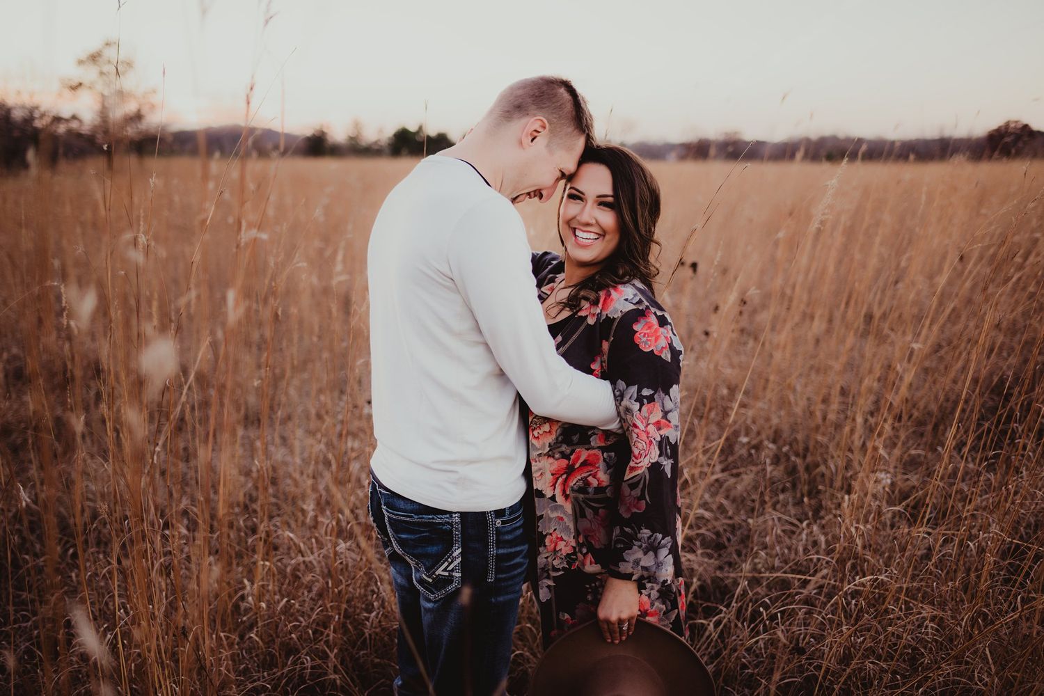A romantic embrace in a golden field at sunset shows a couple sharing an intimate moment.
