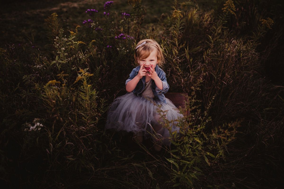 Moody portrait in a wildflower field featuring a tulle dress and playful expression.