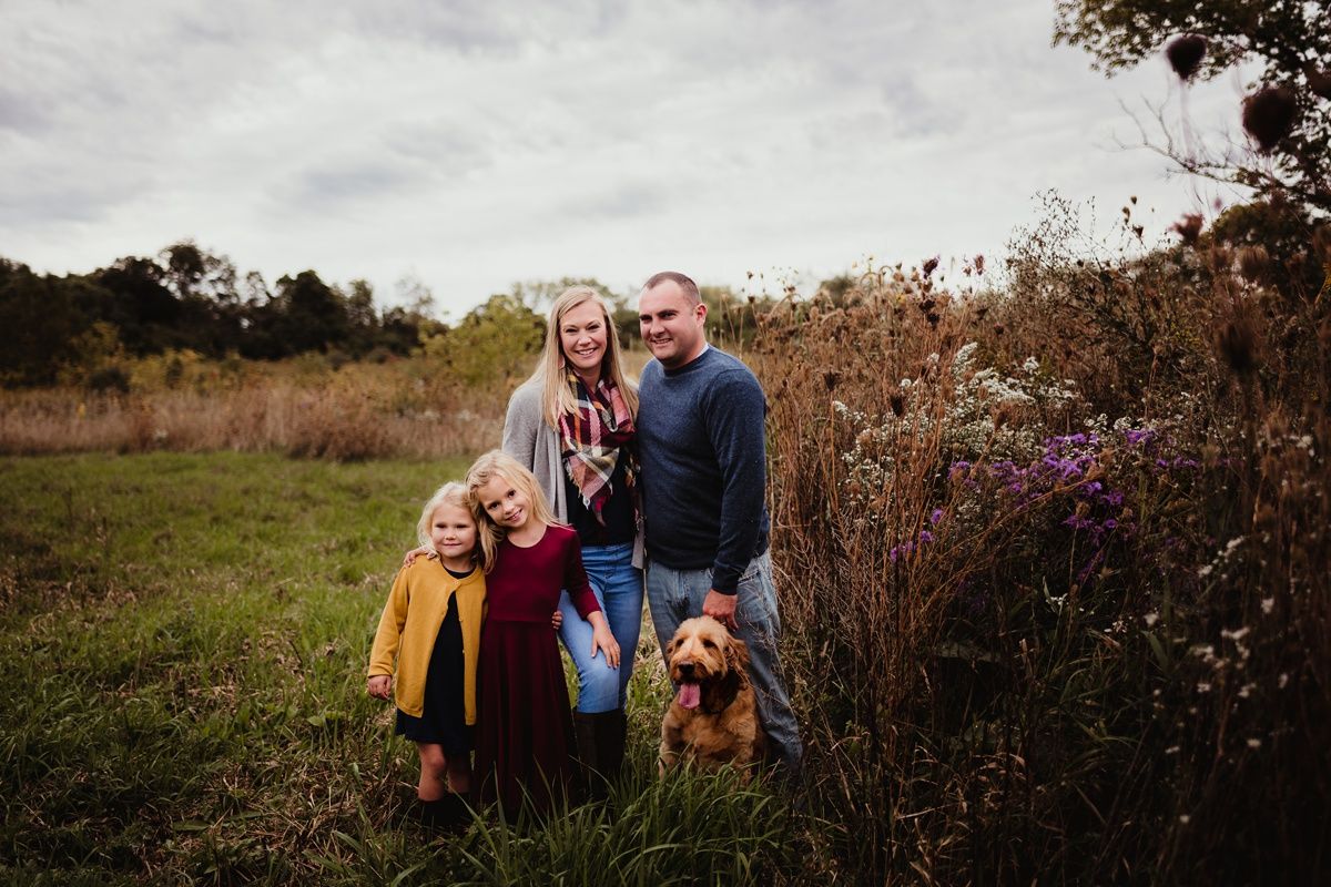 A group photo in a fall field with wildflowers and two dogs.
