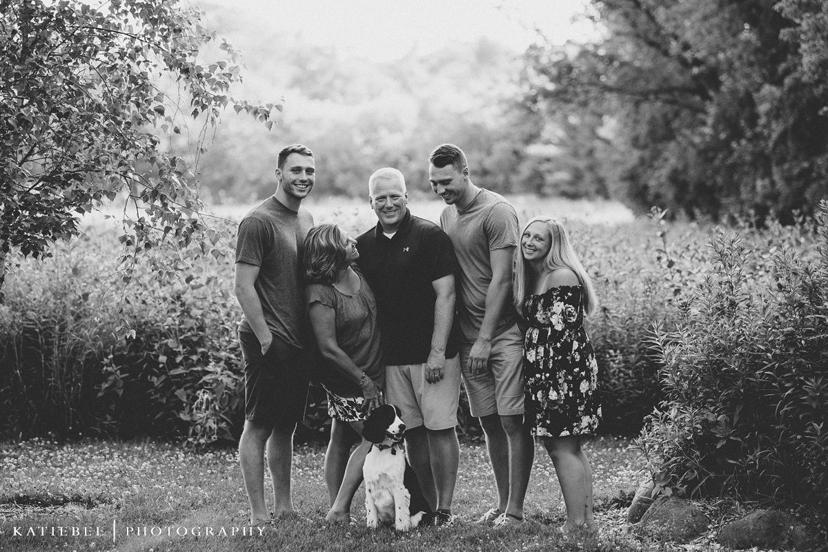 A black and white outdoor family portrait with a small dog in a field of wildflowers.