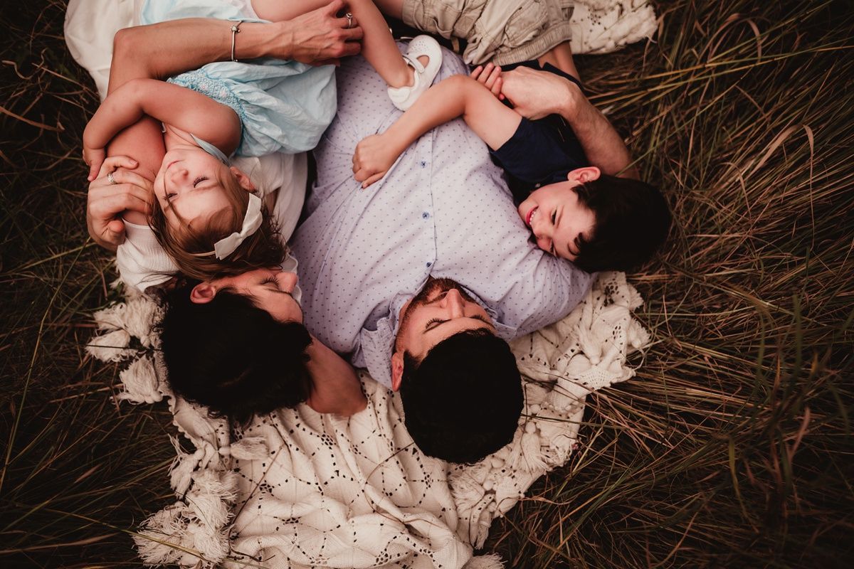 Family lying together on blanket in tall grass during outdoor photoshoot.