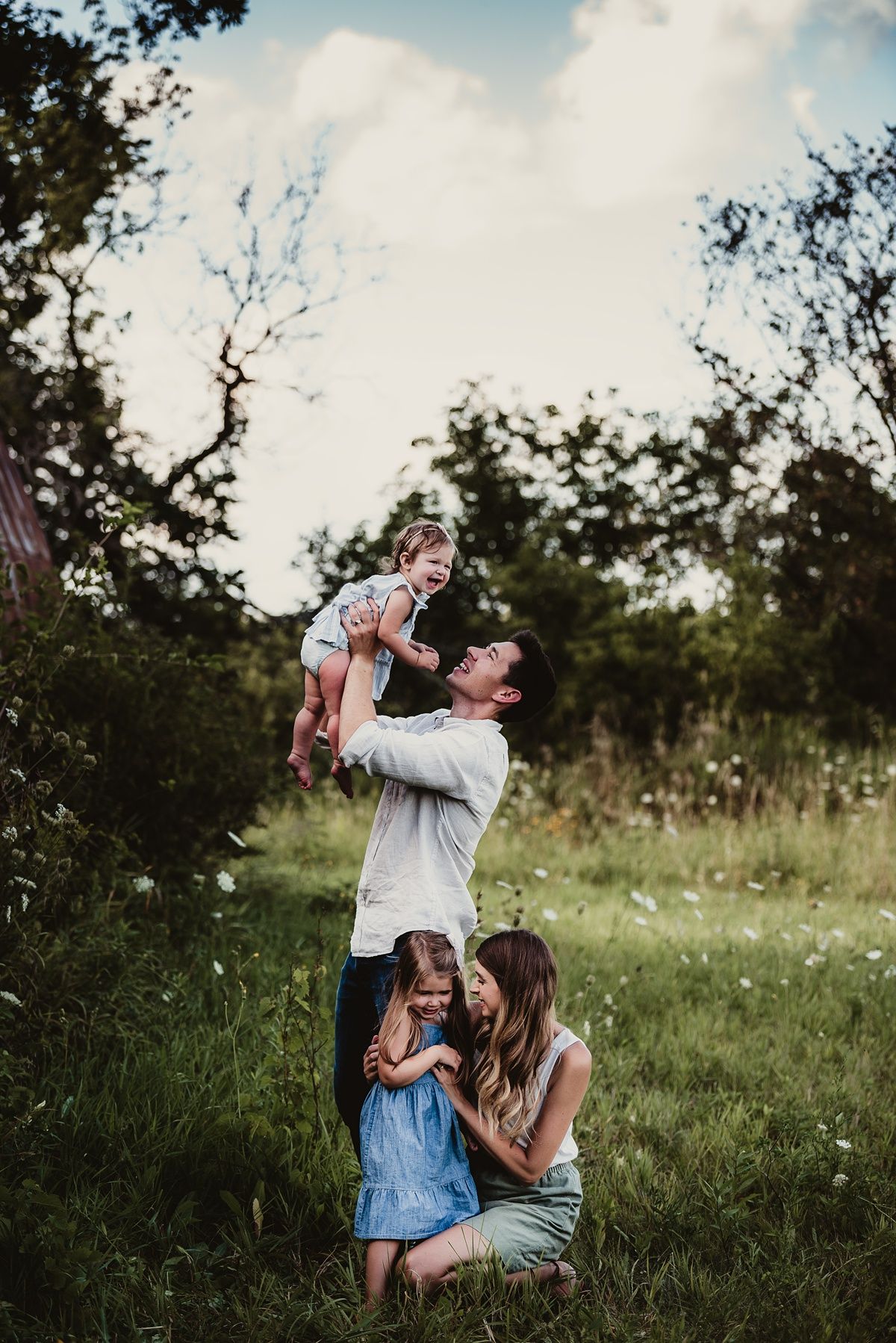 A playful family moment captured outdoors with lifted children and embraces.