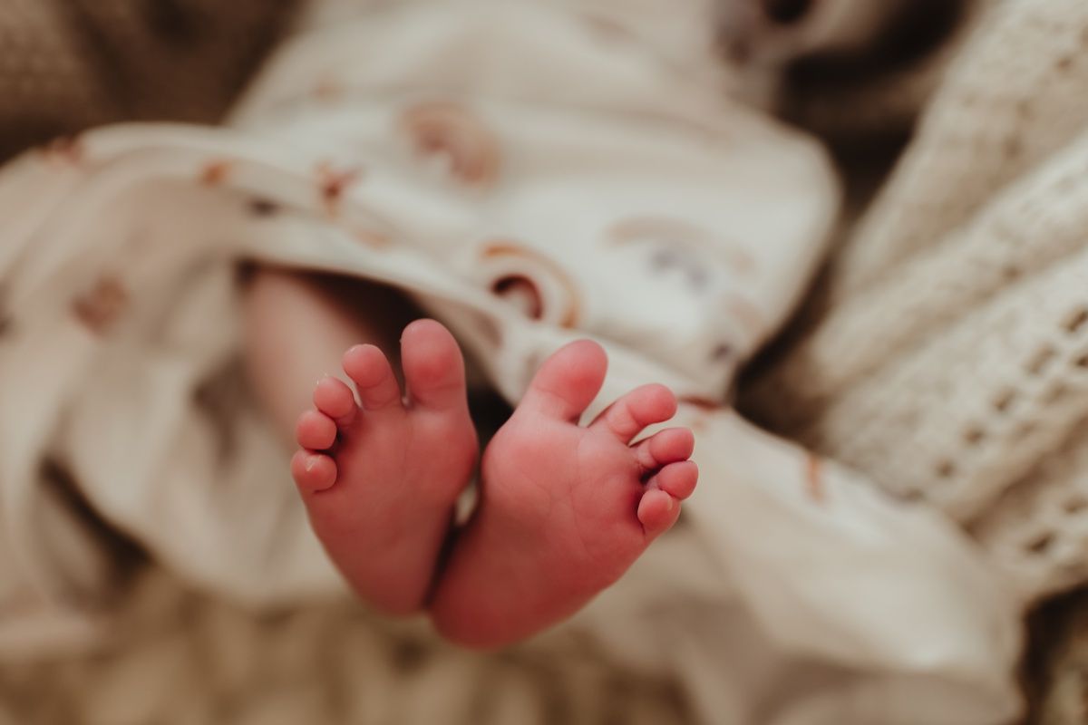 Close-up of tiny newborn baby feet against soft beige blankets.