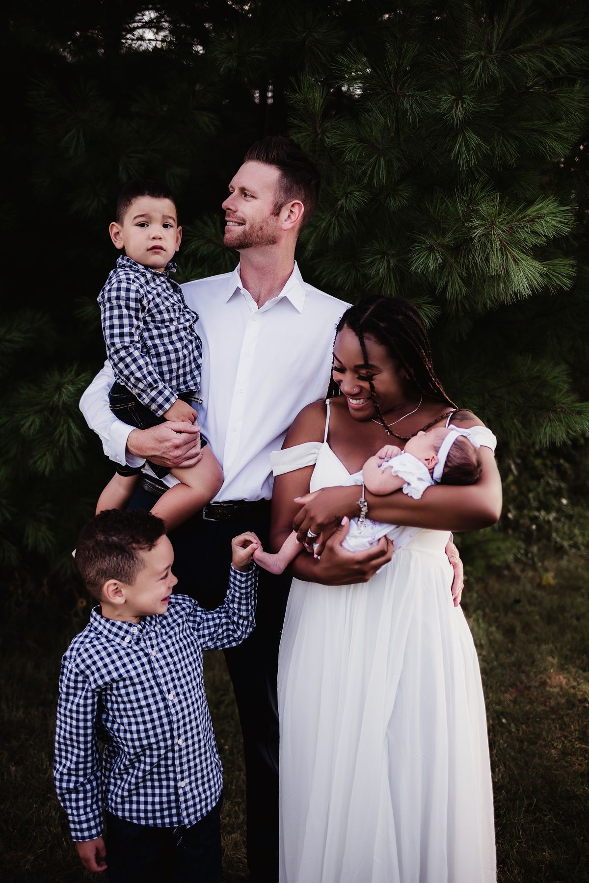 Happy family portrait outdoors with children in matching shirts and newborn baby.