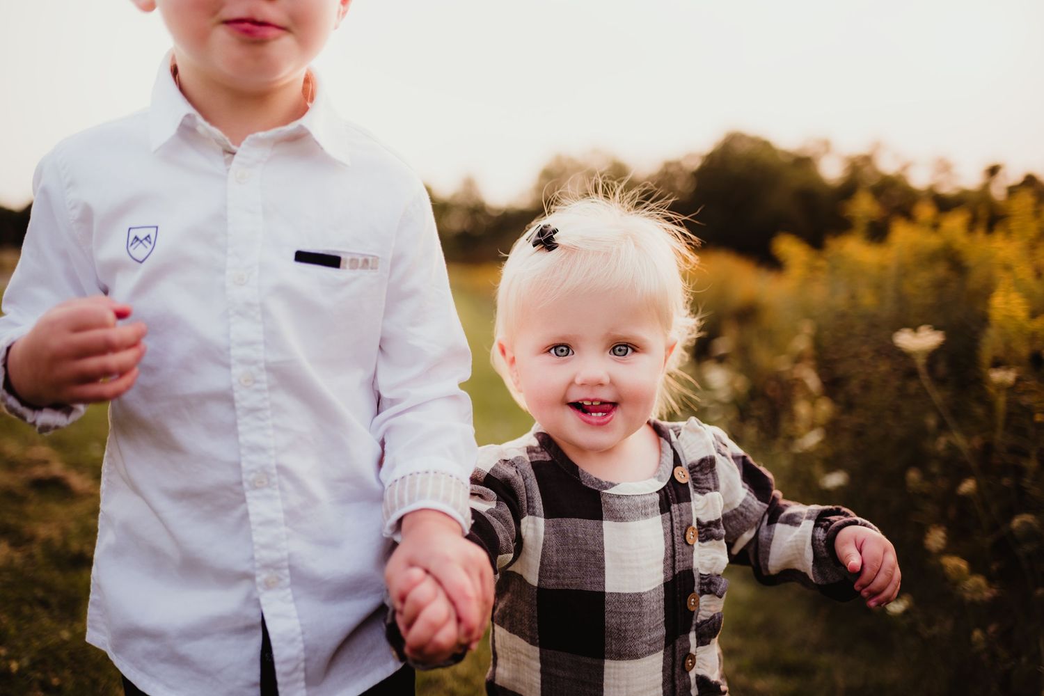 Two children holding hands outdoors during golden hour.