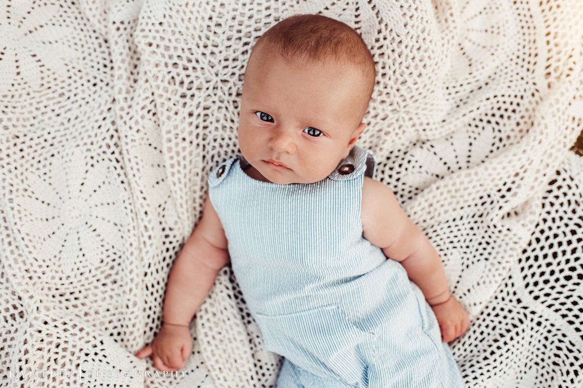 Baby wearing light blue outfit lying on white lace blanket.