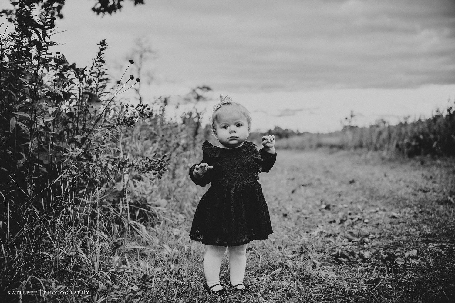 Black and white photo of small child in dress standing on outdoor path.