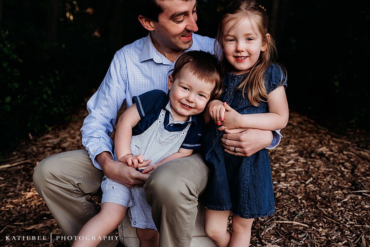 A heartwarming outdoor family portrait set against a natural dark background.