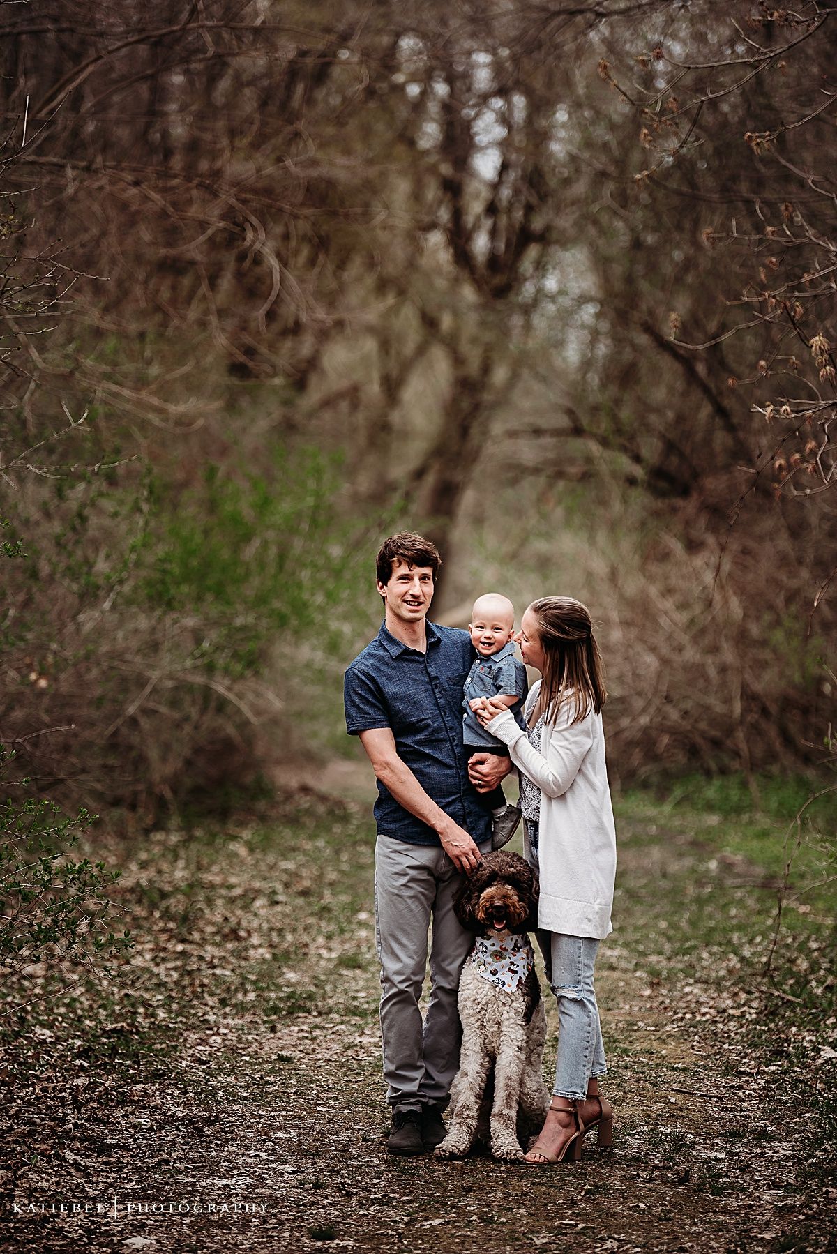 Family of three with their spotted dog posing on woodland path.