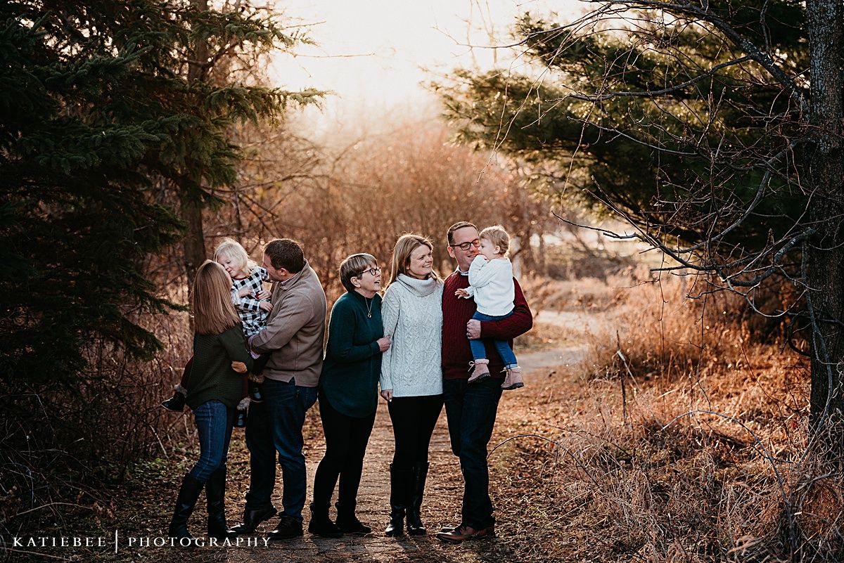 Candid outdoor family photo session with pine trees and warm sunset lighting in the background.