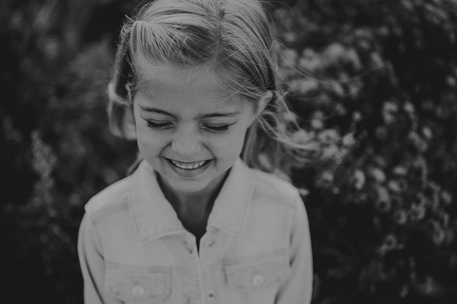 Black and white portrait capturing a genuine smile and relaxed pose outdoors.