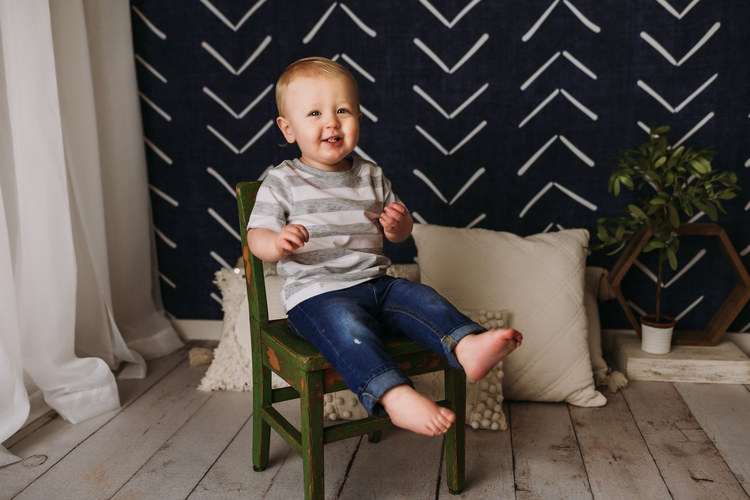 A small child sits on a vintage green chair against a black and white patterned backdrop.