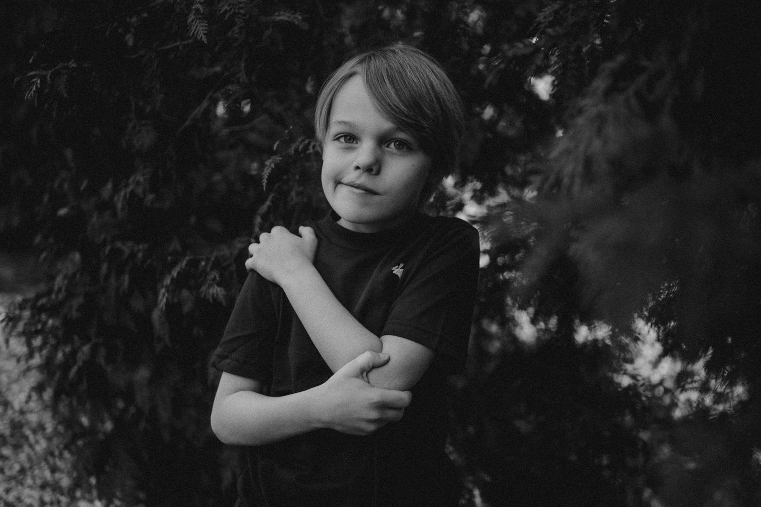 Black and white portrait of child in dark shirt against foliage background.