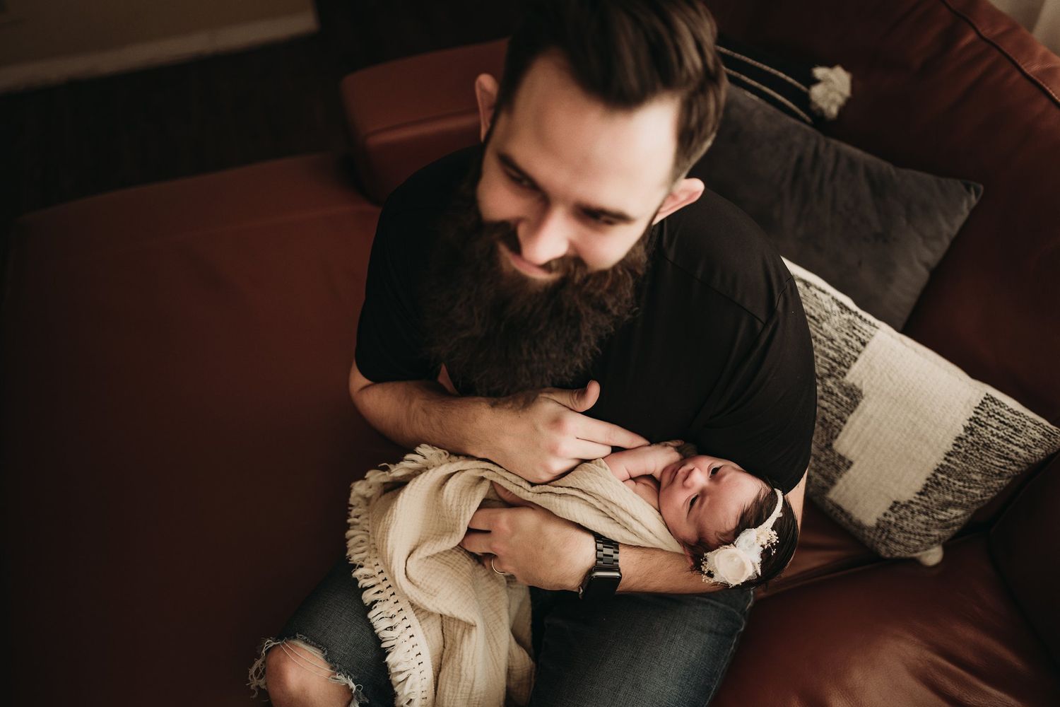 Parents lovingly hold their newborn baby while relaxing on a couch in intimate family moment.
