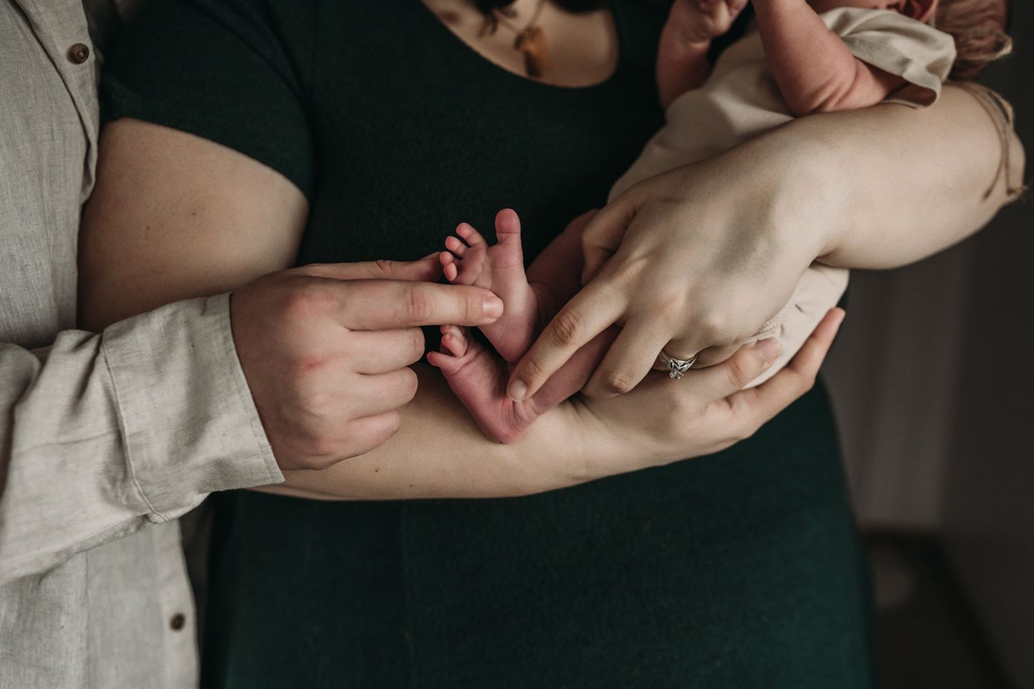 Close-up of hands tenderly holding a tiny newborn's fingers in an intimate moment.