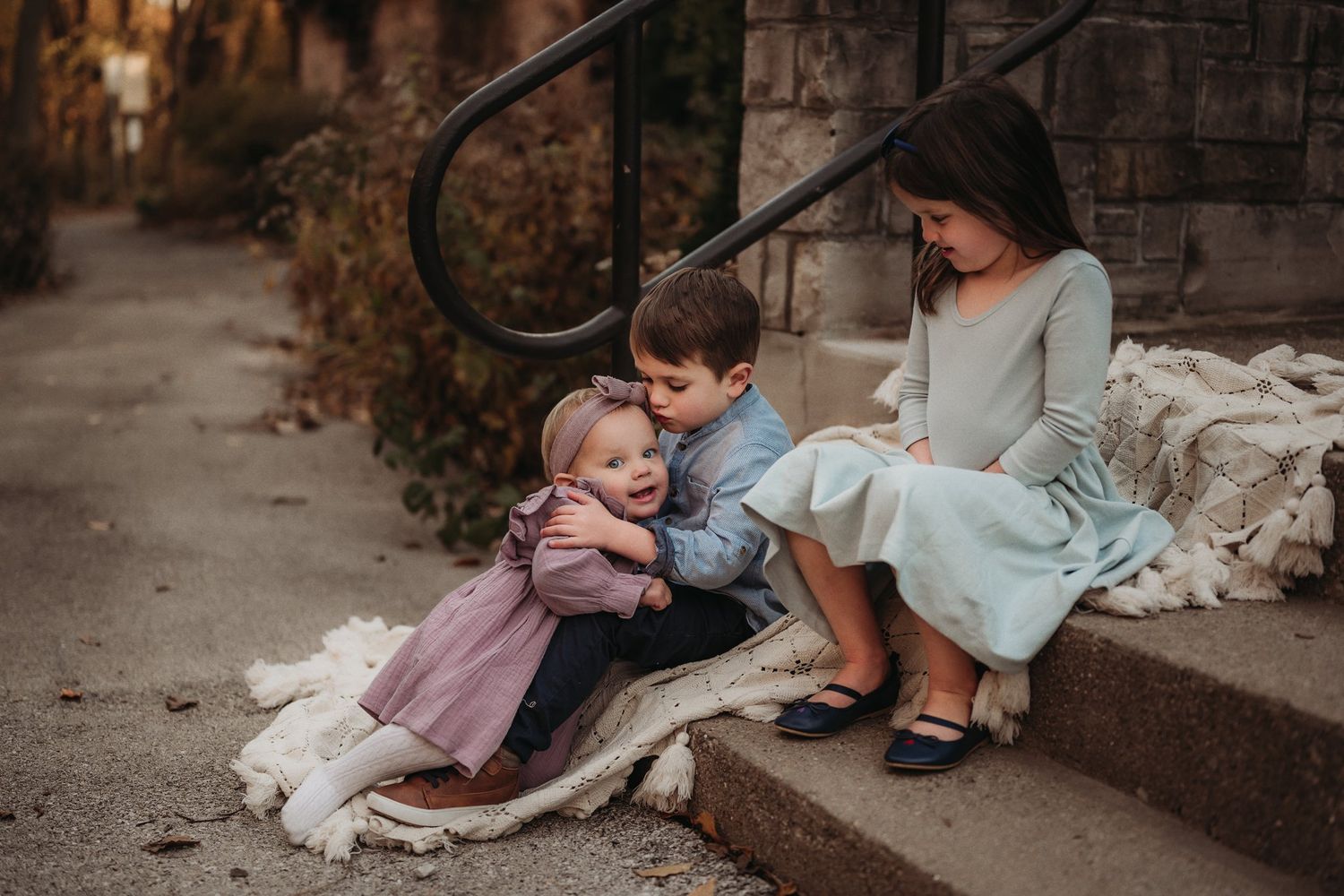 Three people sitting on outdoor steps with cozy white blankets.