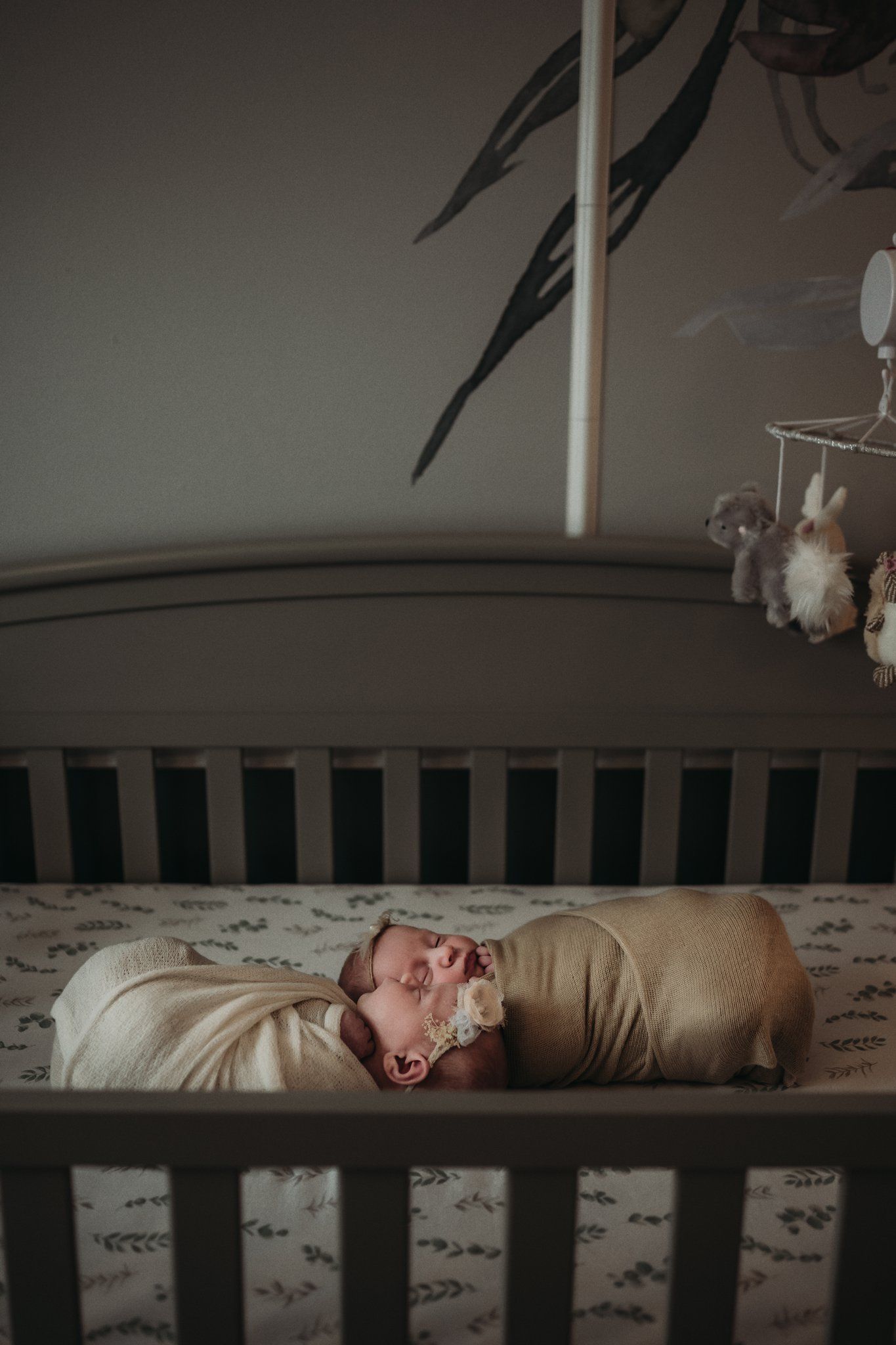 Newborn baby sleeping peacefully in dark wooden crib with mobile hanging above.