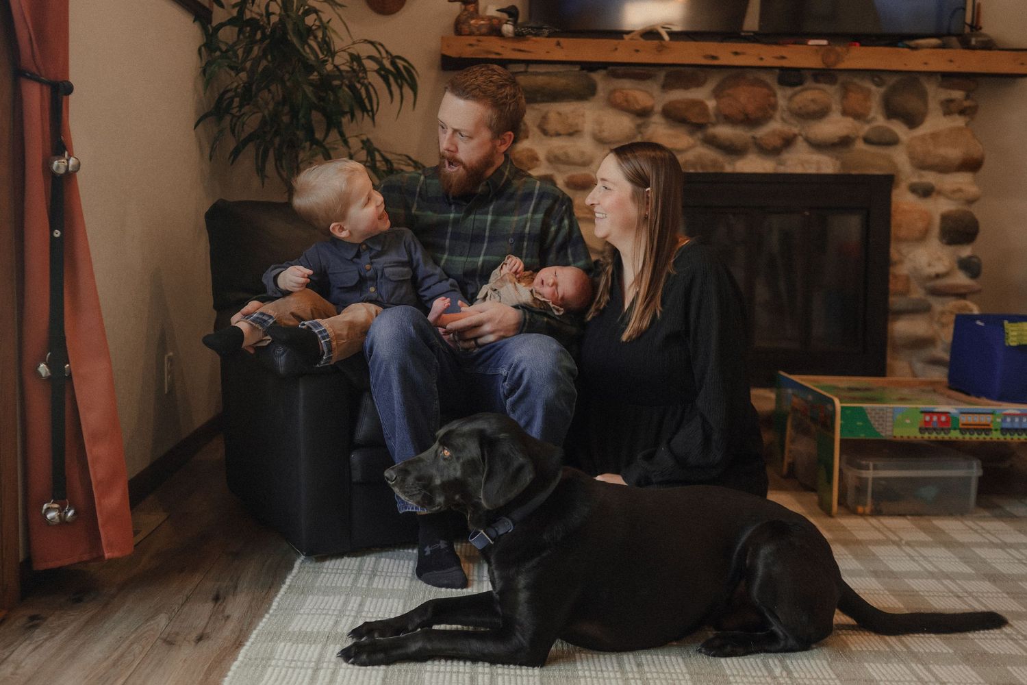 A couple sits close together on a couch in a cozy living room with stone walls and warm lighting.