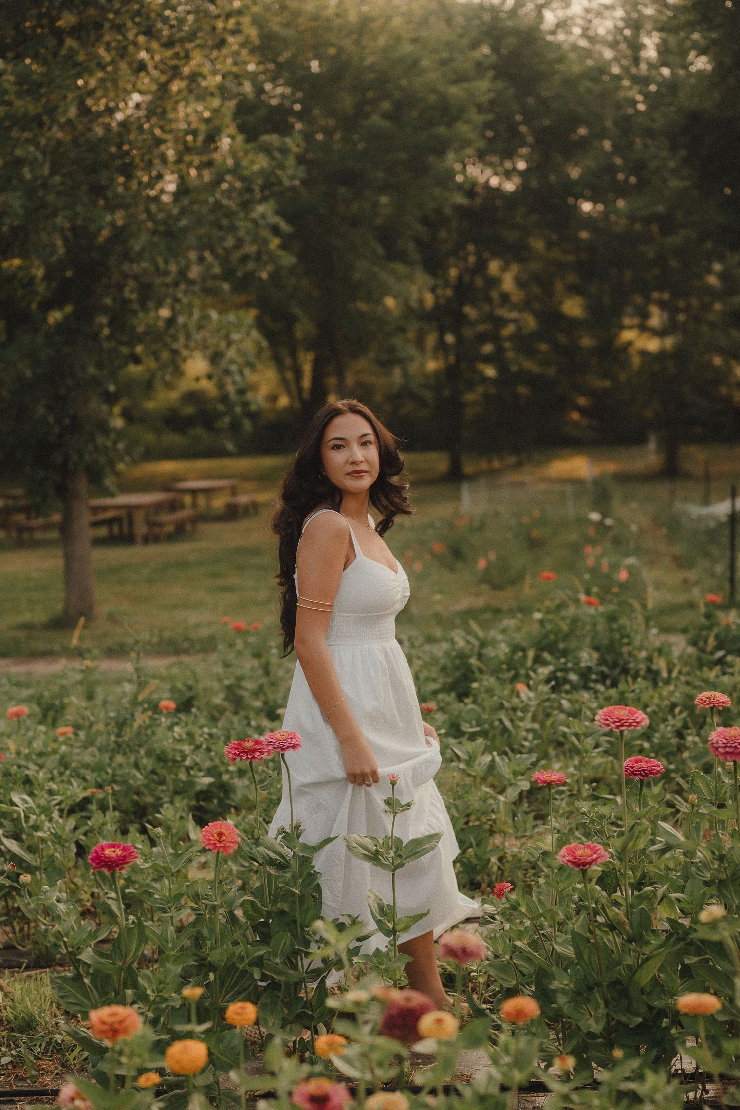 Woman in white dress standing among colorful zinnia flowers in a lush garden at golden hour.