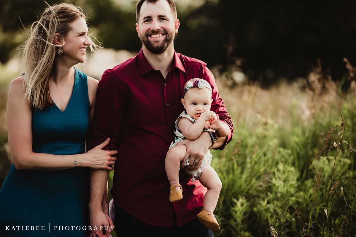 Family portrait in golden meadow wearing coordinated burgundy and teal outfits.