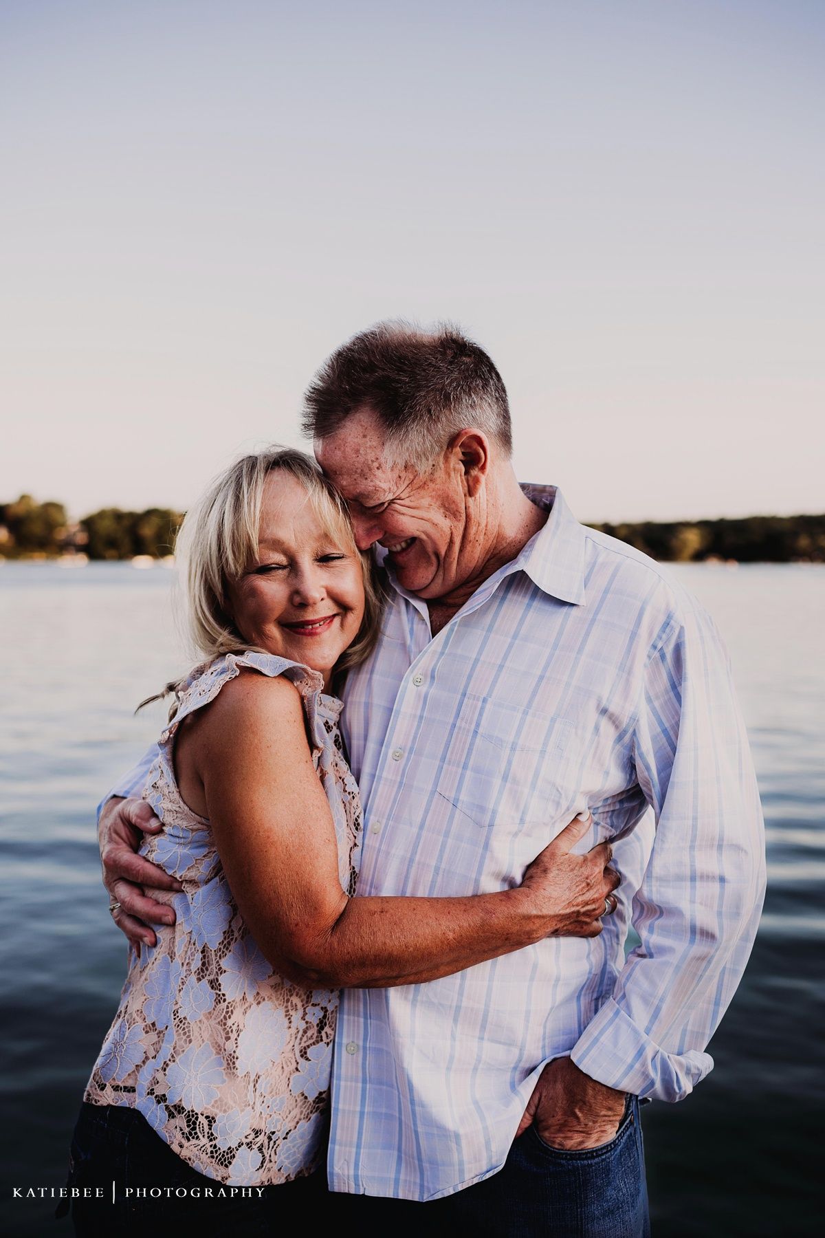 Couple embracing and laughing together near water during sunset photography session.