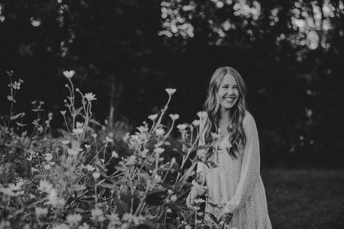 Black and white portrait standing among wildflowers wearing flowing cream dress.
