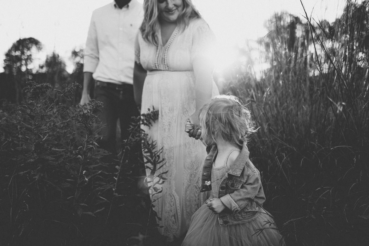 Black and white family portrait taken in a field with dramatic sunlight filtering through tall grass.
