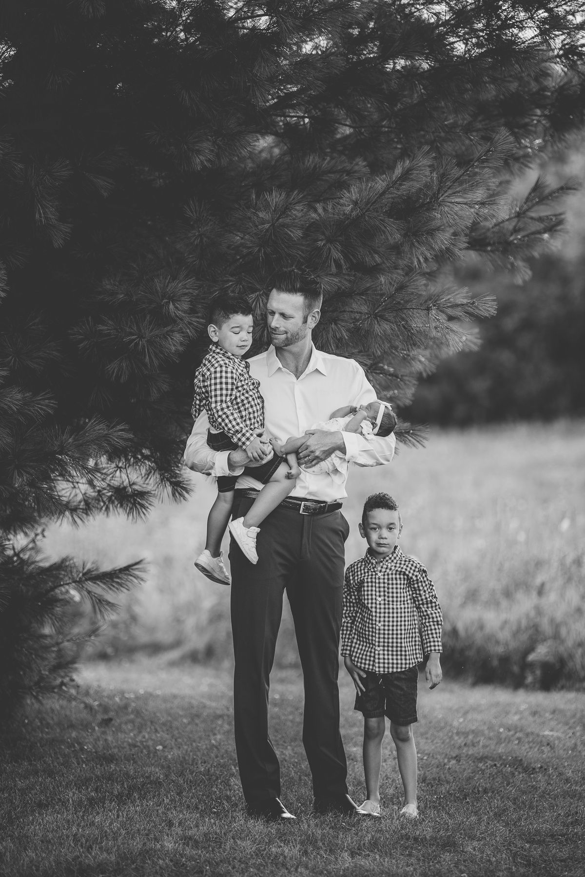 Black and white family portrait against pine trees in a natural setting.