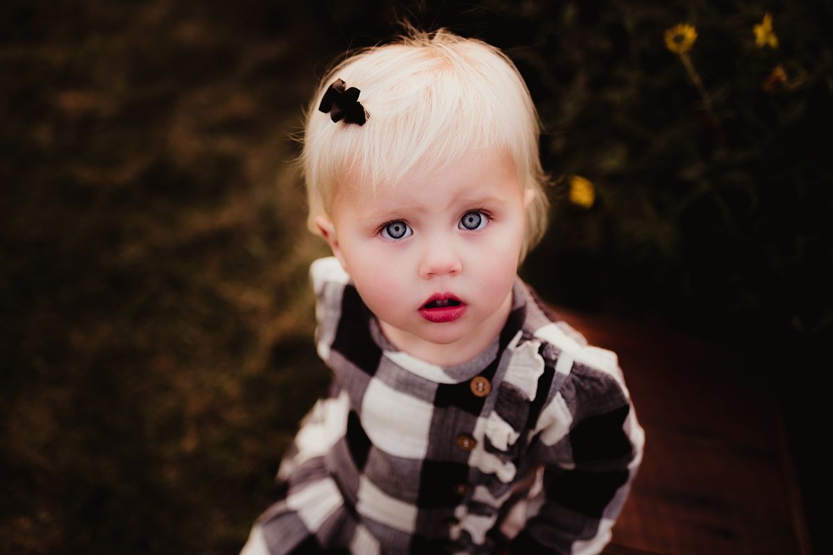 Close up of child in black and white plaid outfit against dark background.