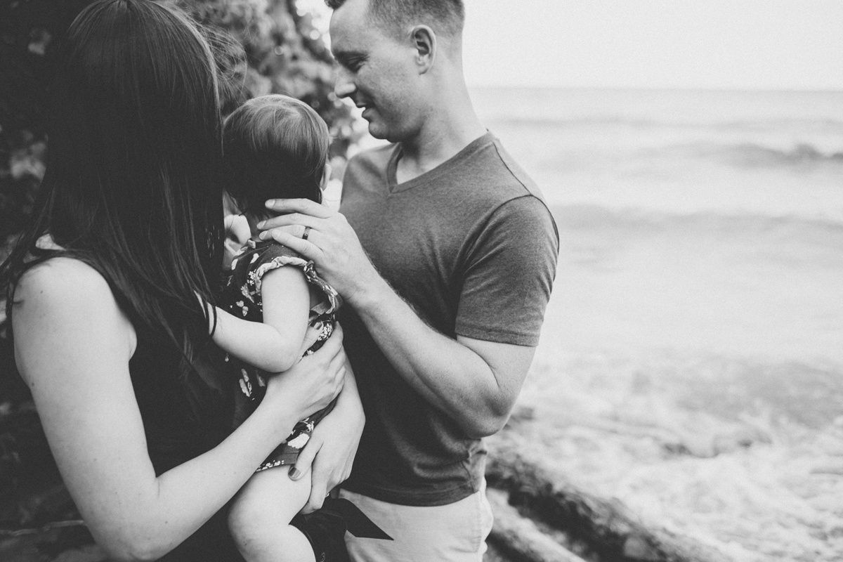A tender black and white family moment captured against an ocean backdrop.