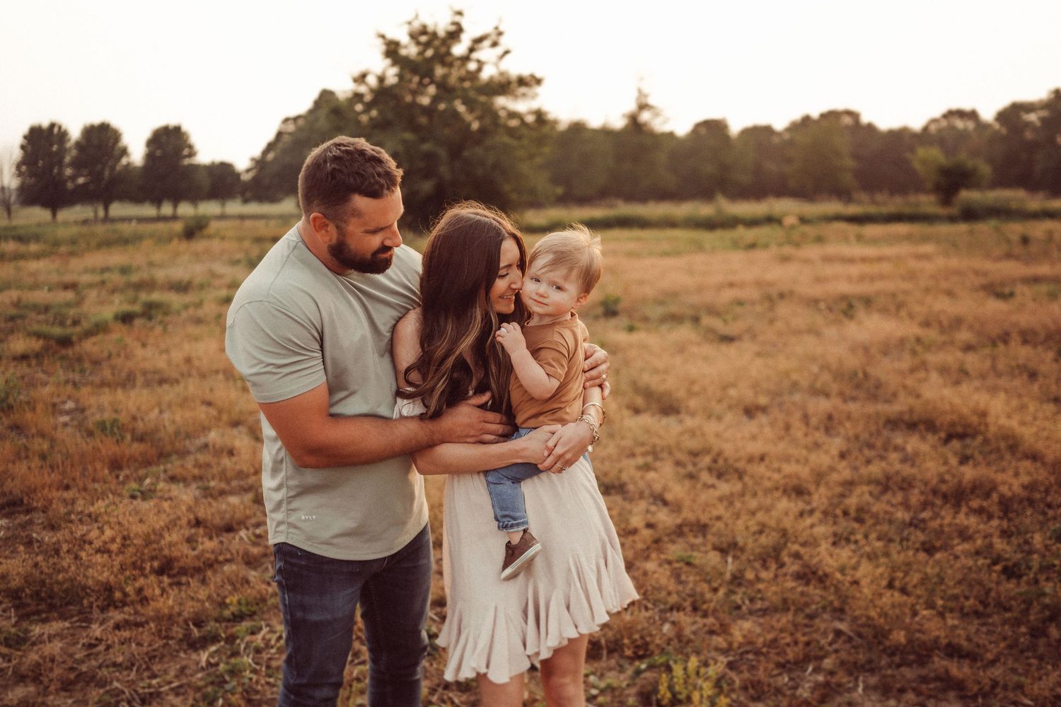 A family embraces while standing in a golden meadow during sunset.