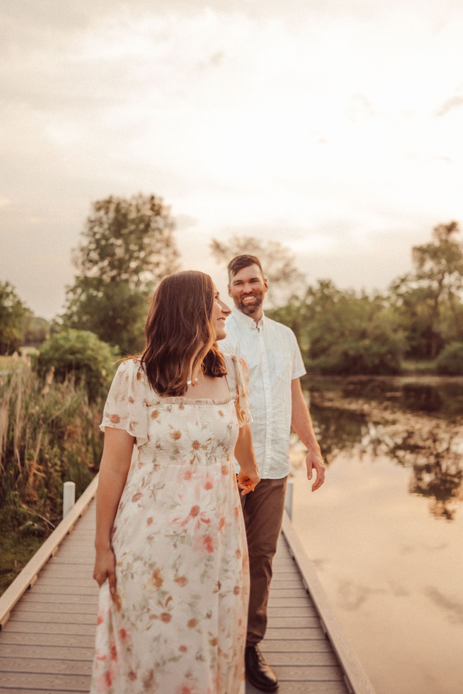 Couple in casual attire walking along a scenic boardwalk at sunset.