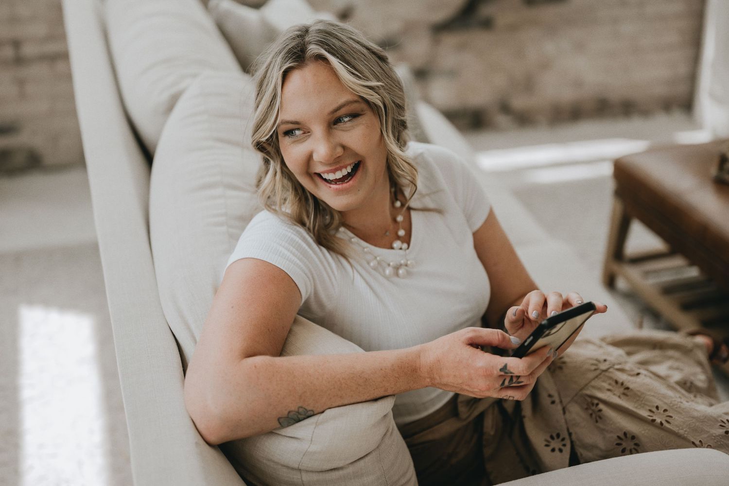 Joyful woman uses mobile device while relaxing on white sofa.