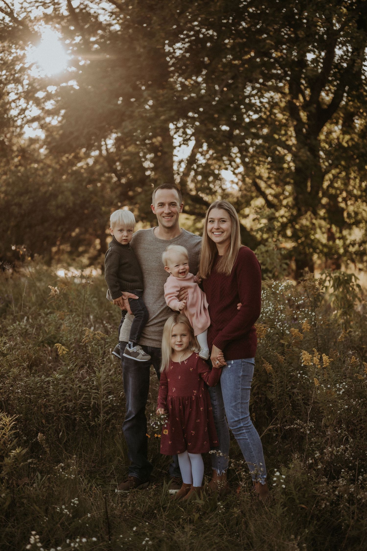 Autumn family portrait in woodland setting with golden sunlight filtering through trees.