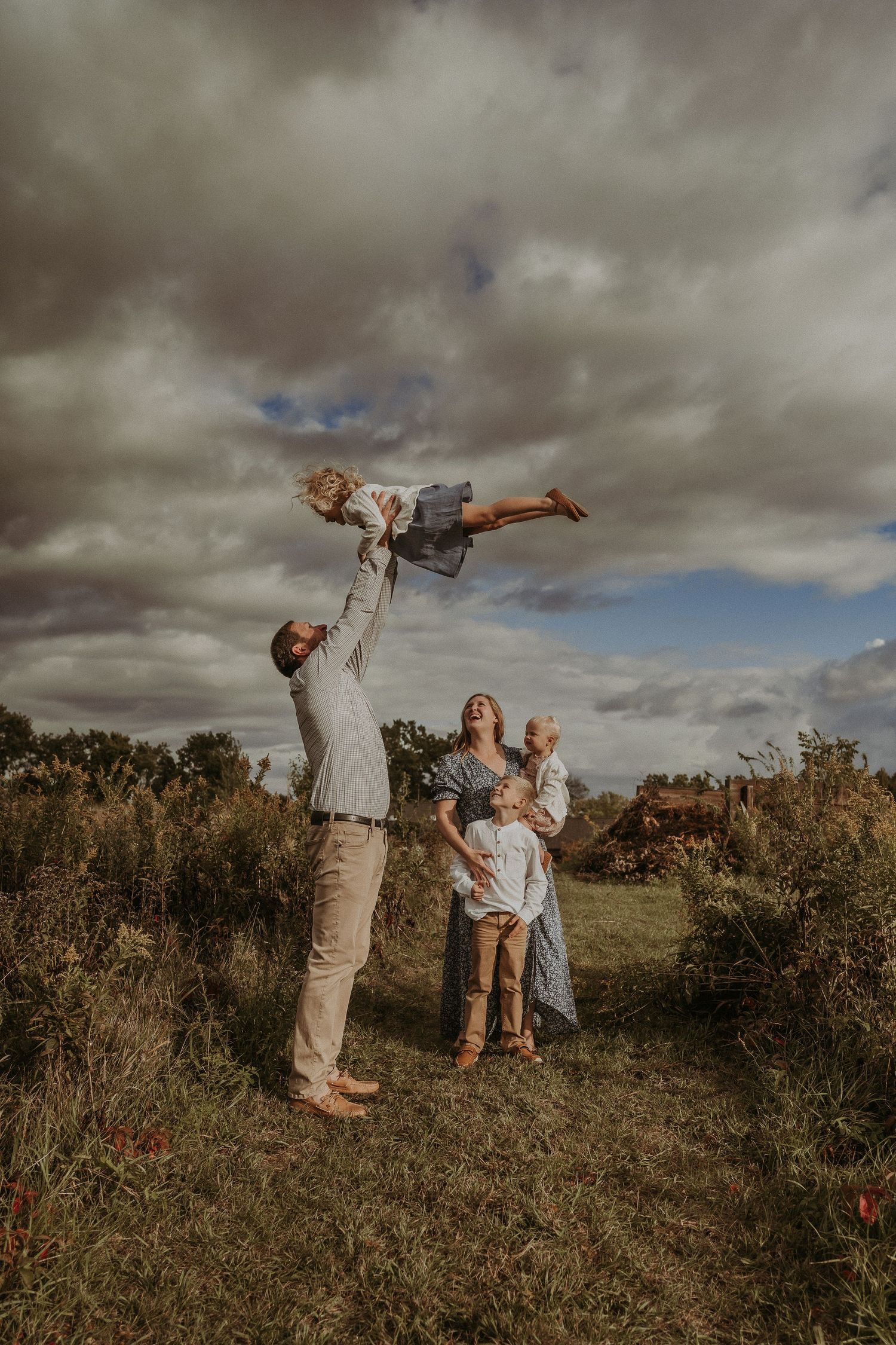 Playful family moment captured outdoors with dramatic sky and natural landscape.